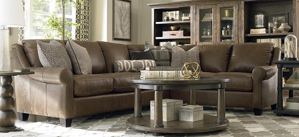 luxury living room featuring brown leather wraparound sofa with round wooden table and wooden end tables with honeycomb pattern area rug