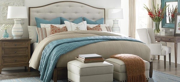 luxury home furniture bedroom with light blue, white, and rust colored bedding with brown furniture and white ottomans